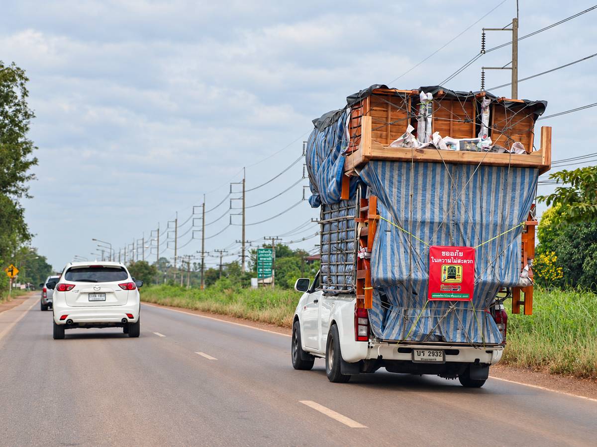 Hoch mit Möbeln beladener Pickup und weitere Autos auf einer Straße in Thailand