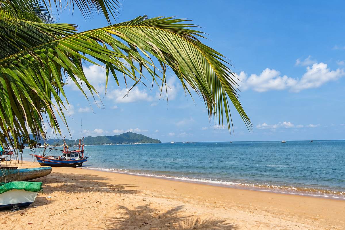 Palmenstrand mit Fischerboot und Blick auf eine Insel in Thailand